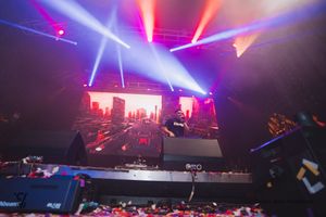 Colorful laser lights and beams illuminate a dark concert venue with silhouettes of the crowd visible below.