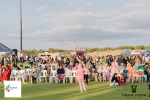 A panoramic view of an outdoor wedding ceremony setup with white chairs arranged on a grassy lawn near the beach.
