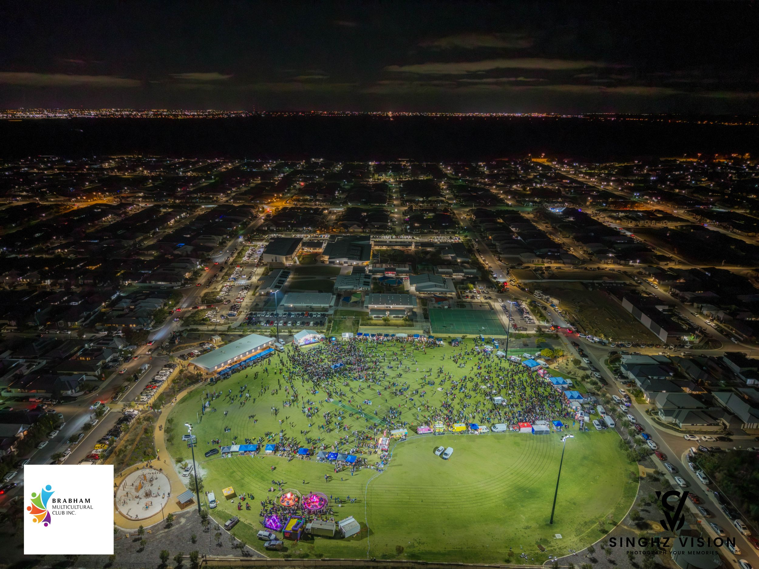 Aerial night view of multiple soccer fields with bright stadium lights illuminating green turf and surrounding urban area.