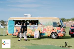 Colorful vintage camper vans and trailers parked in a row on grassy field during a summer festival.