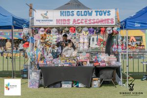 Outdoor vendor booth displays colorful kids toys and accessories under a blue tent at a community event.