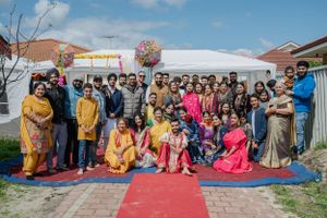 Group photo at outdoor cultural celebration with colorful traditional attire and red carpet on sunny day.