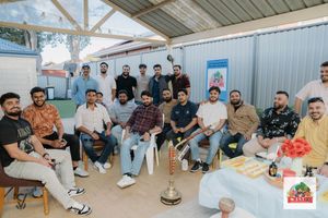 A panoramic view of people gathered for an outdoor meal around long tables under a covered patio area.