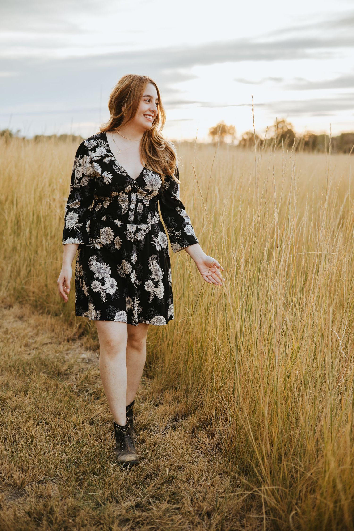 A high school senior walking through tall grass gently touching the strands and looking off into the horizon