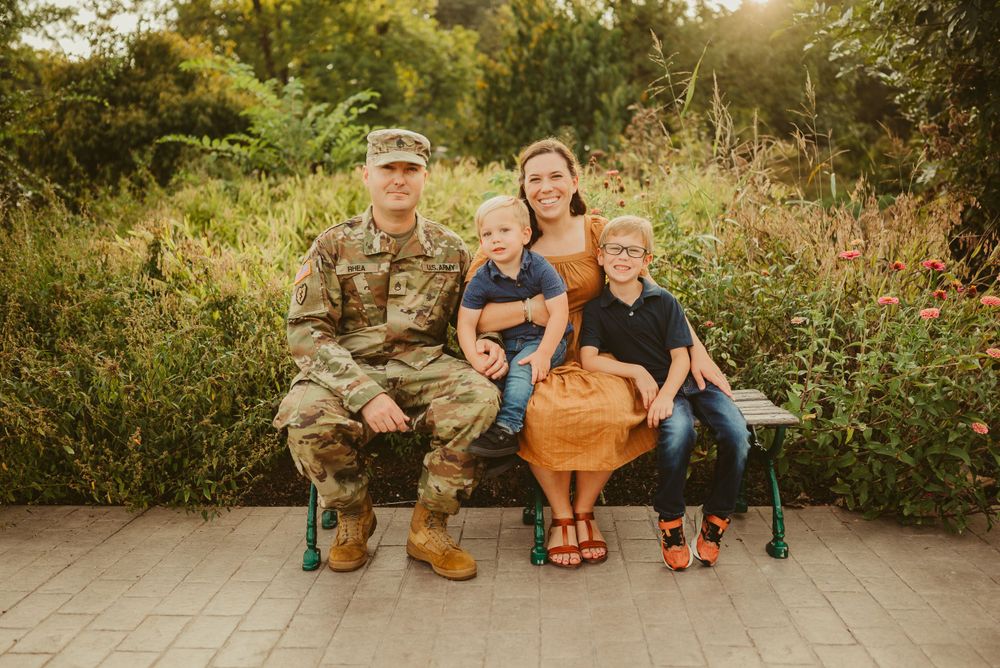 Fort Campbell military family sits smiling on bench during photos at Dunbar Cave State Park, Photo by Disney Magic Photography.