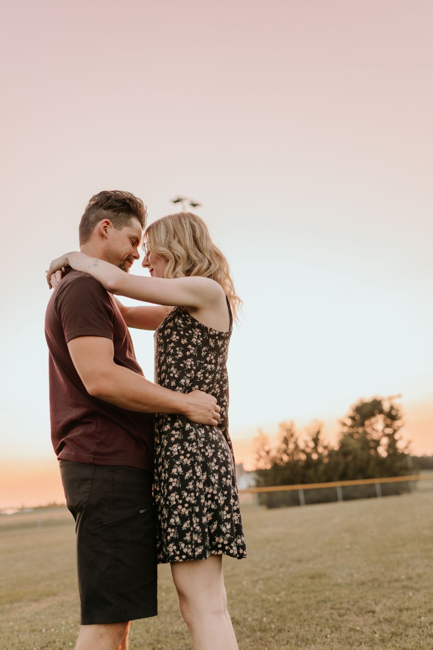 Romantic couple embracing while sitting against tree trunk in golden field.