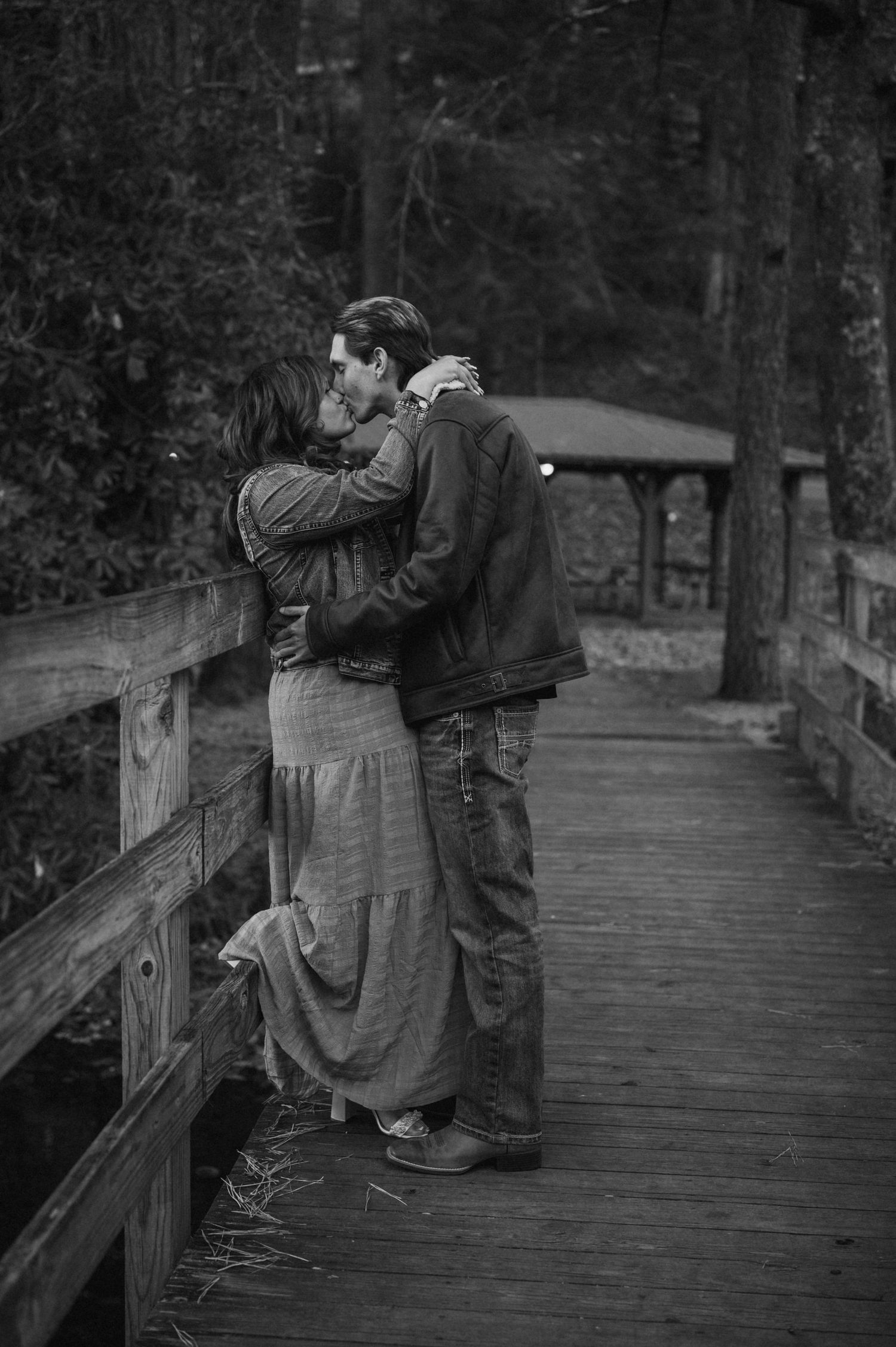 A couple embraces on a wooden bridge in a moody forest setting.