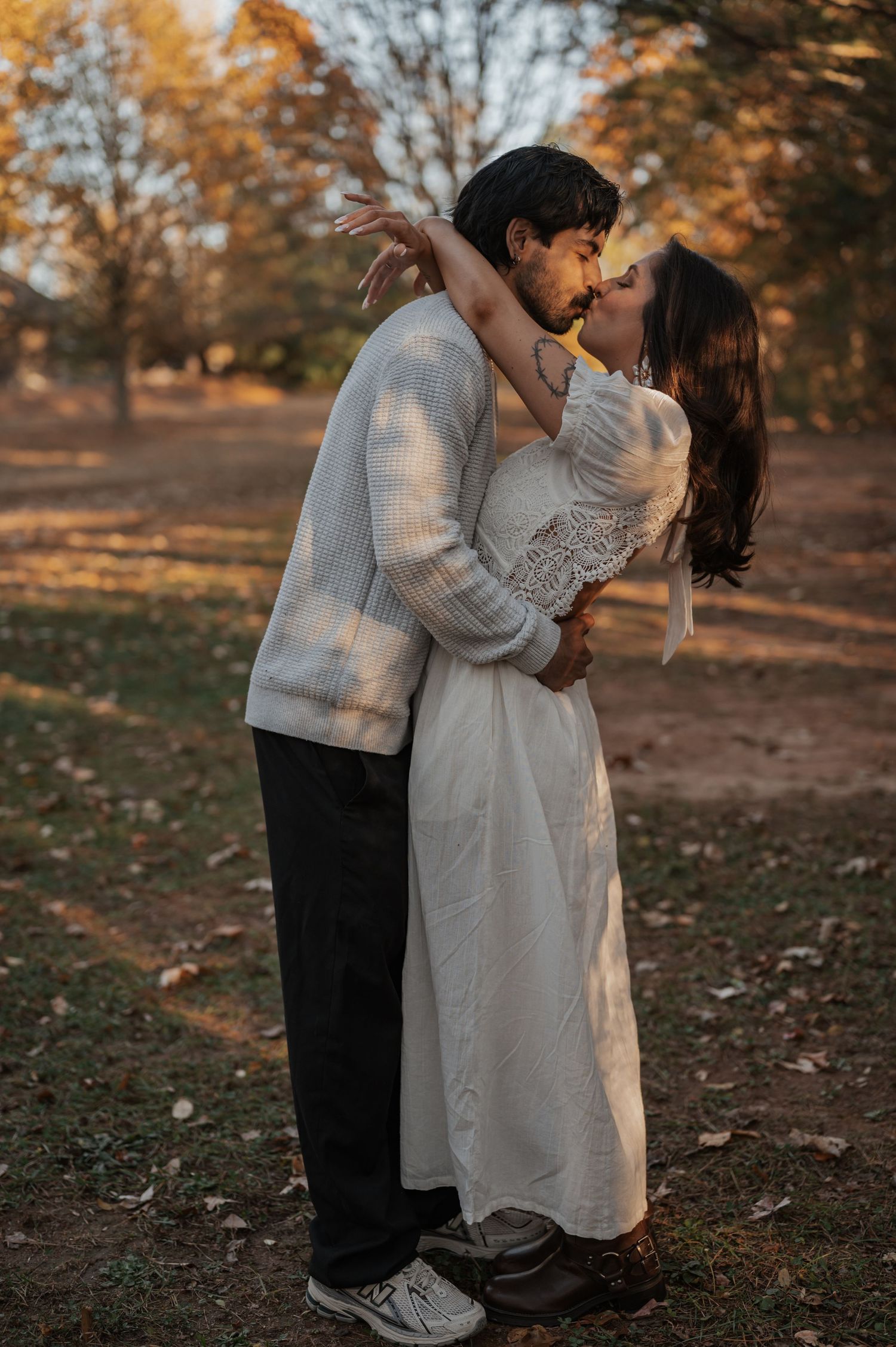 Romantic autumn photoshoot featuring a couple in white dress and sweater embracing in golden sunlight.