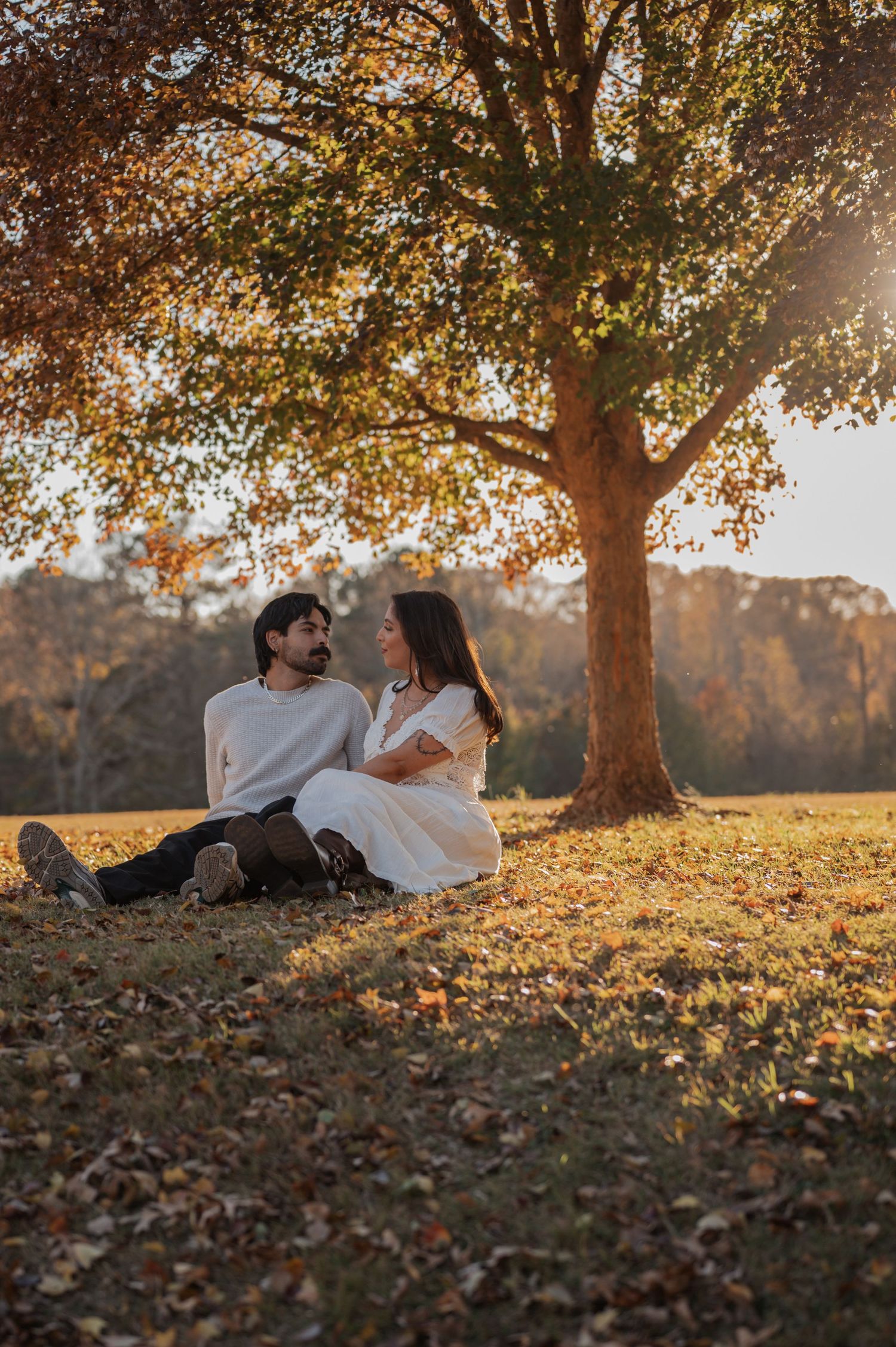 Couple relaxing together under fall trees during sunset golden hour photo session.