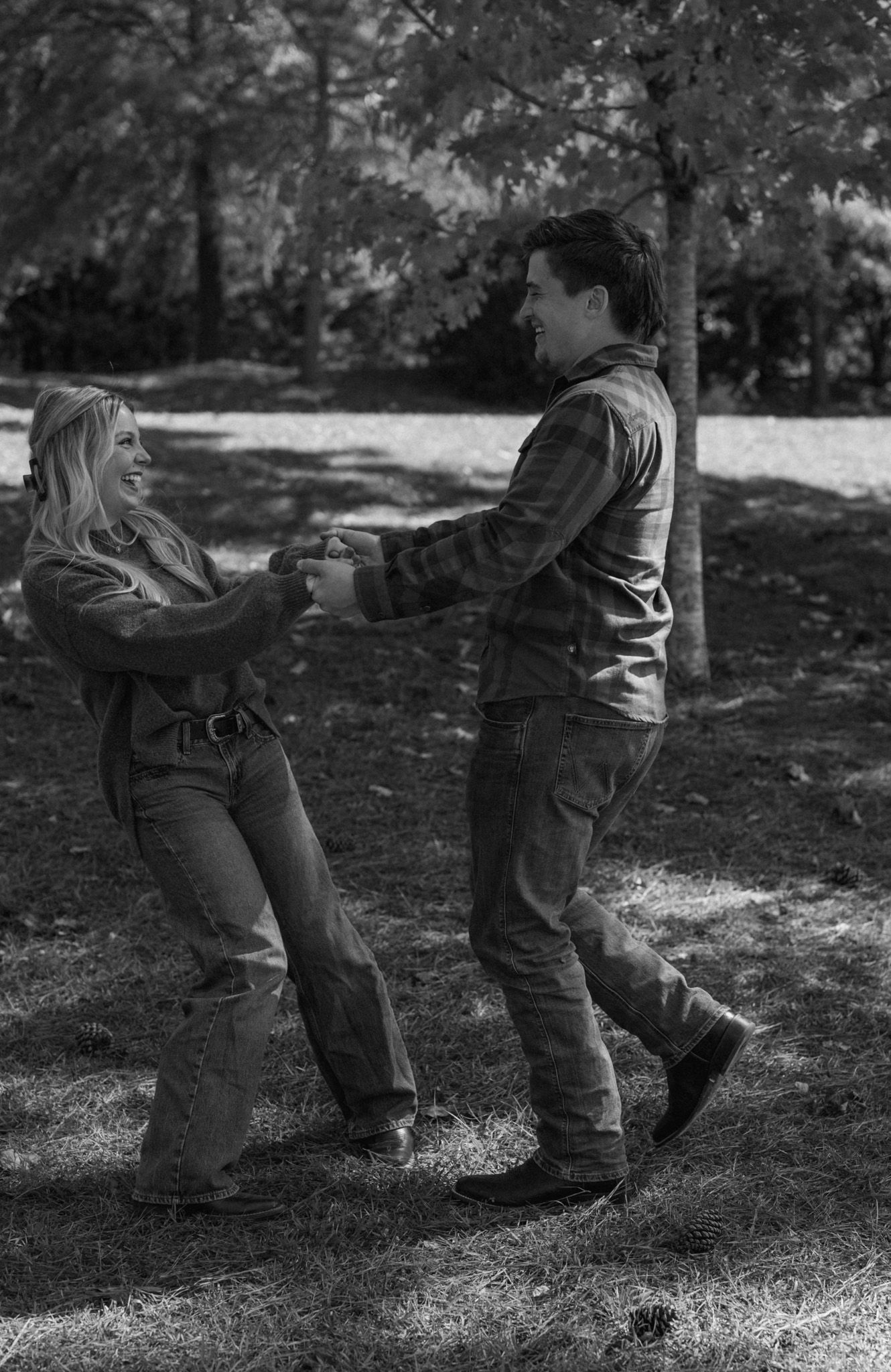 Playful black and white photos of a couple dancing and twirling in a park setting.