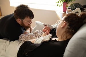 Sioux City, Iowa photographer. New parents gazing lovingly at their swaddled newborn baby in a warm, sunlit hospital room.