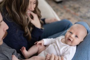 Sioux City, Iowa photographer. New parents smile lovingly at their alert newborn baby during an intimate in-home photo session.
