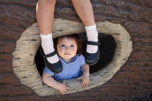 Sioux City, Iowa photographer. Adorable baby in blue dress and white socks looking up through a heart-shaped hole in a wooden log.