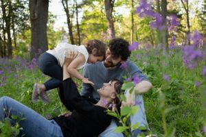 Sioux City, Iowa photographer. Family of three plays joyfully in a field of purple wildflowers during golden hour in the forest.