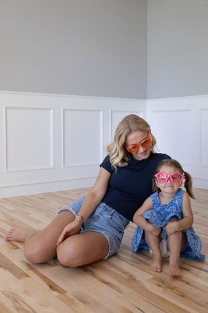 Sioux City, Iowa photographer. Blonde mother and young daughter sitting on hardwood floor wearing matching pink star-shaped sunglasses.