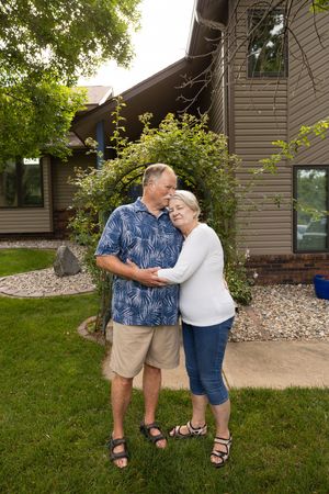 Sioux City, Iowa photographer. senior couple embracing and smiling together in front of their home surrounded by green landscaping.