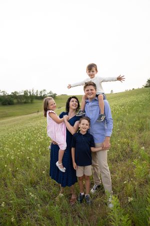 Sioux City, Iowa Photographer. family of five posing in a green meadow with wildflowers, parents with kids including one on dad's shoulders.