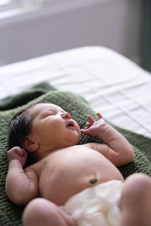 Sioux City, Iowa photographer. Newborn baby lying on a green knit blanket with eyes slightly open and tiny hands raised.