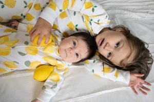 Sioux City, Iowa photographer. Two babies in matching yellow lemon print pajamas lying together on a white bed.