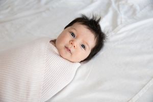 Sioux City, Iowa photographer. Alert dark-haired baby swaddled in a pink striped blanket lying on white bedding.
