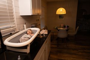 Sioux City, Iowa photographer. Swaddled newborn baby resting in a bassinet on a kitchen counter in a warmly lit home.