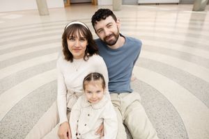 Sioux City, Iowa photographer. Happy family of 3 with young daughter sitting together on a circular patterned floor in a bright building.