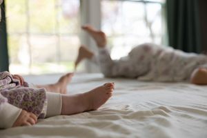 Sioux City, Iowa photographer. Two young children relaxing on a white bed, captured in a soft natural light close-up of their bare feet.