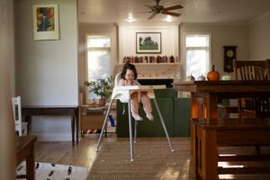 Sioux City, Iowa photographer. Young child sitting in a high chair in a bright home dining room with green sofa.