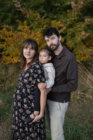 Sioux City, Iowa photographer. Portrait of a pregnant woman, bearded man, and young child outdoors in fall foliage.