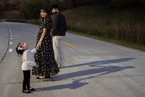 Sioux City, Iowa photographer. Family of three holding hands on an empty road surrounded by autumn trees.