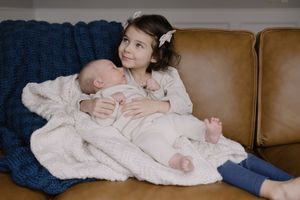 Sioux City, Iowa photographer. Young girl sitting on leather sofa lovingly holding newborn baby sibling.