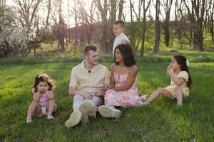 Sioux City, Iowa photographer. Interracial family of five sitting together on green grass in sunny park.