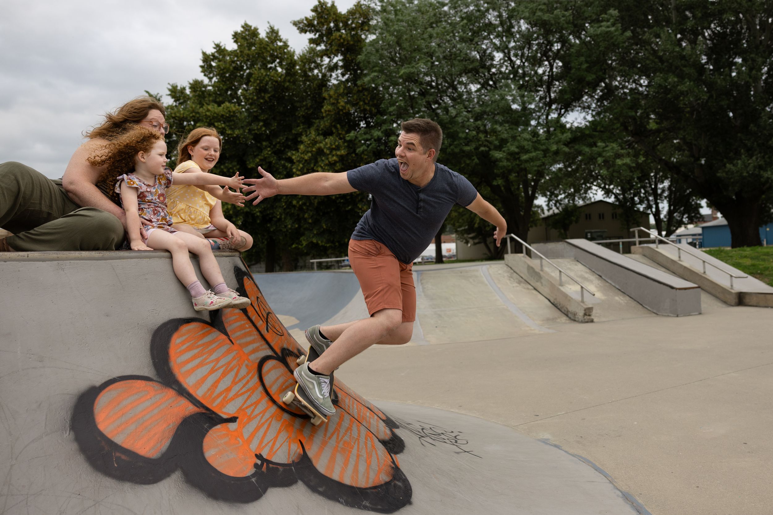 Family playing at a skatepark with a colorful butterfly mural painted on the ground on a sunny day.