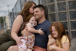 A happy family of four sharing a warm embrace outdoors, featuring two redheaded girls and their smiling parents.