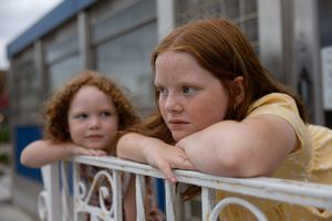 Two red-haired freckled girls leaning on a white railing, looking contemplative outdoors.