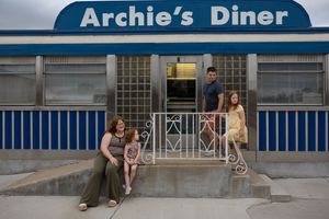 Family poses outside Archie's Diner, a retro blue and white restaurant facade.