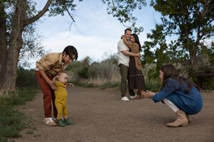 Family of five enjoying an outdoor walk on a dirt path surrounded by trees, with toddler taking first steps.