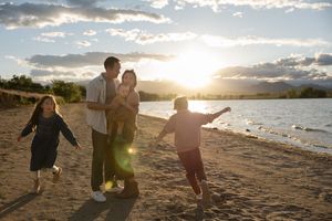 Family enjoying a sunset beach walk with children playing by the water’s edge in golden evening light.