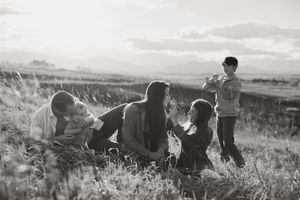 Black and white photo of a family playing together in a grassy field with mountains in the background.