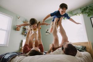 Sioux City, Iowa photographer. Two children airplane lifted by parents playing on a bed in a light green bedroom.