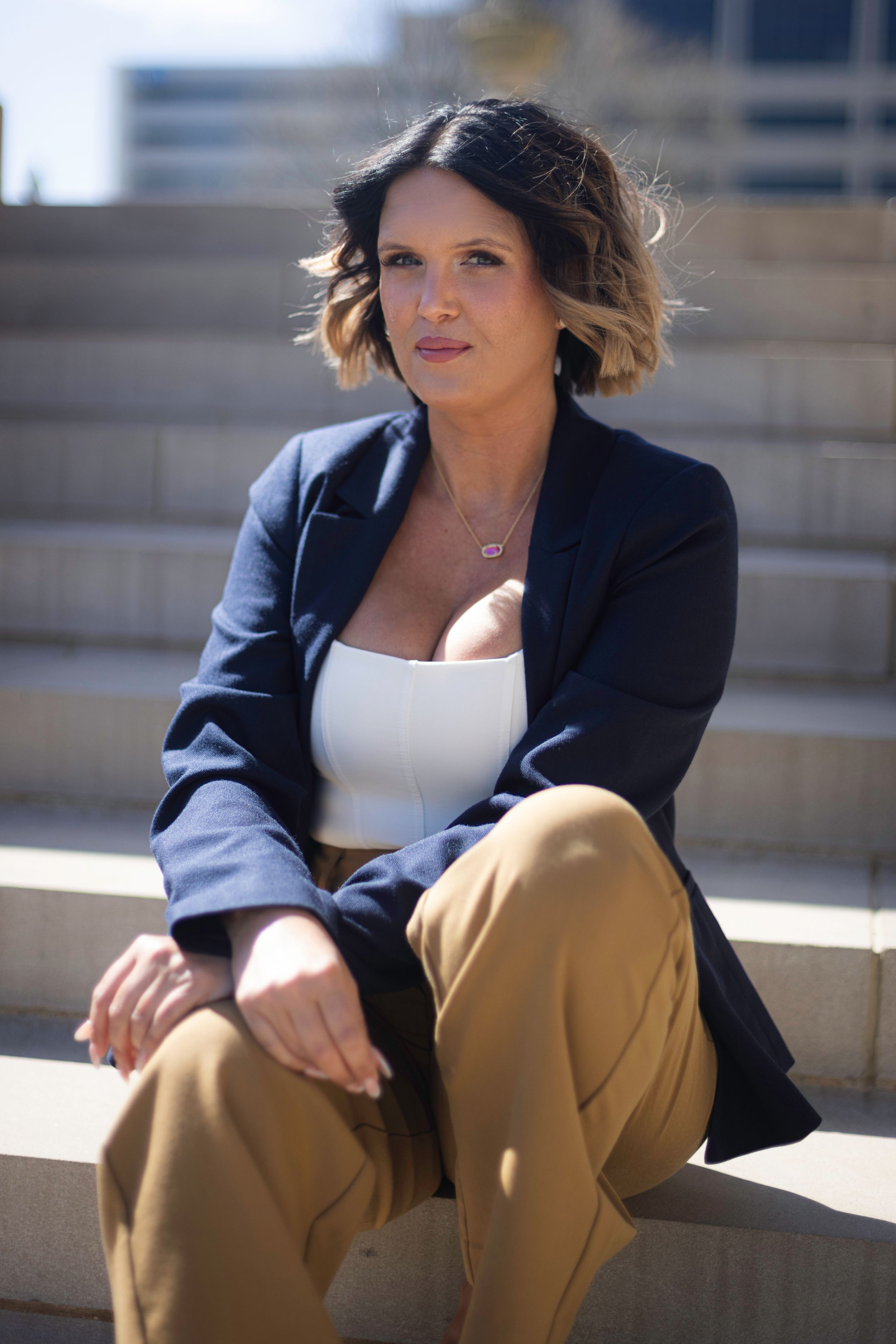 Professional portrait of someone in a navy blazer and tan pants sitting on concrete steps.