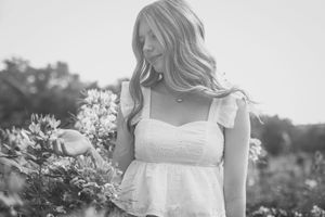 Black and white portrait of someone in a white summer dress holding flowers in a garden setting at sunset.