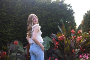 A person in a blue dress poses in a garden with vibrant red canna lilies and tropical foliage in the background.
