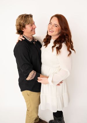 Couple shares joyful laughter during casual photo session against white backdrop.