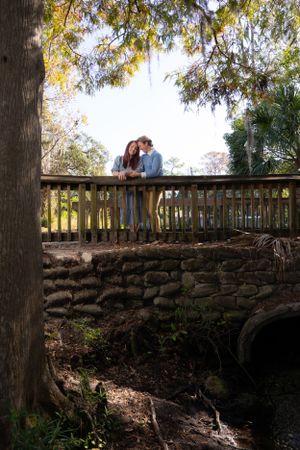 Romantic outdoor portrait by stone wall with trees creating natural lighting and ambiance.