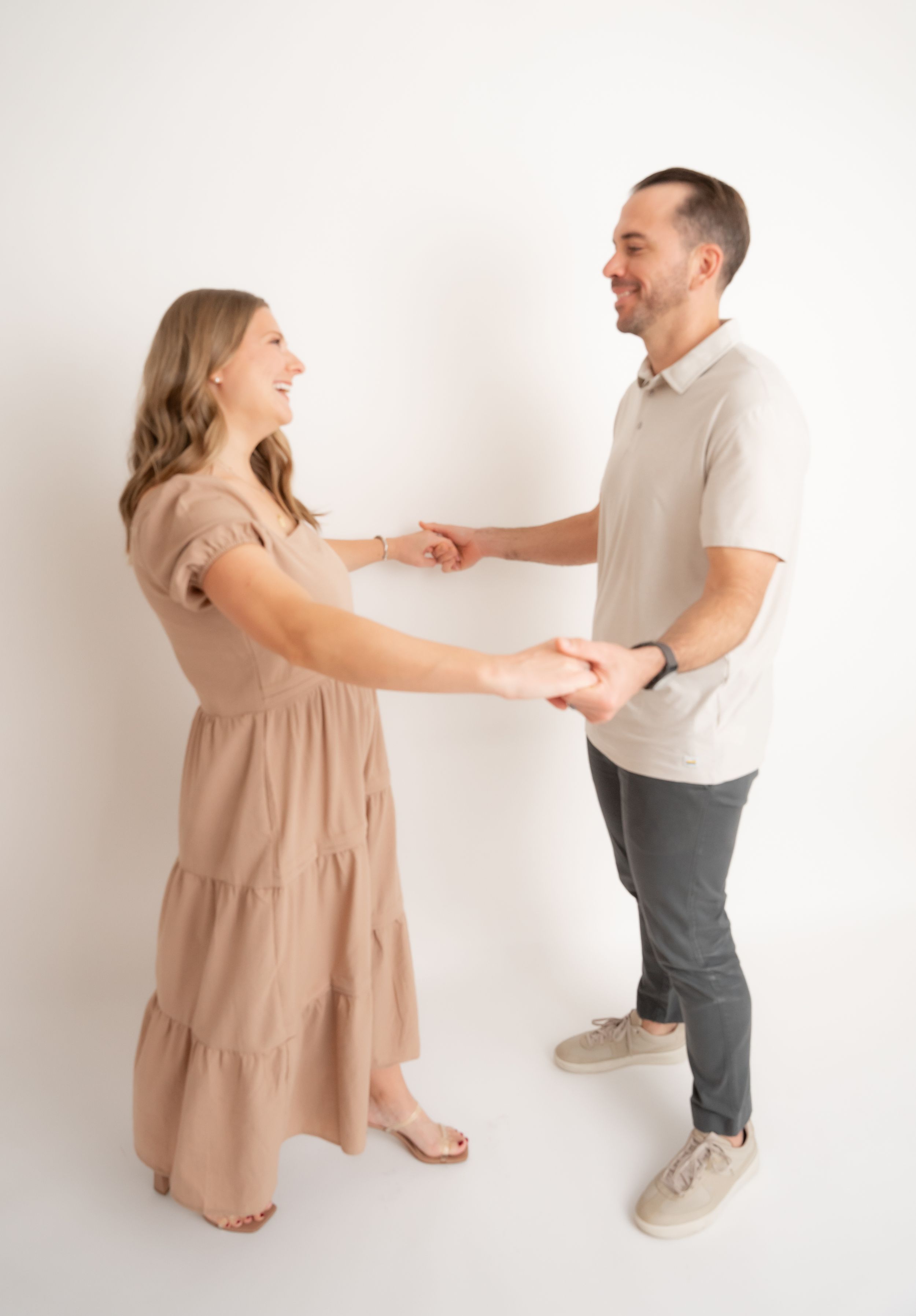 Dancing couple in neutral tones twirls and spins during studio photo session.