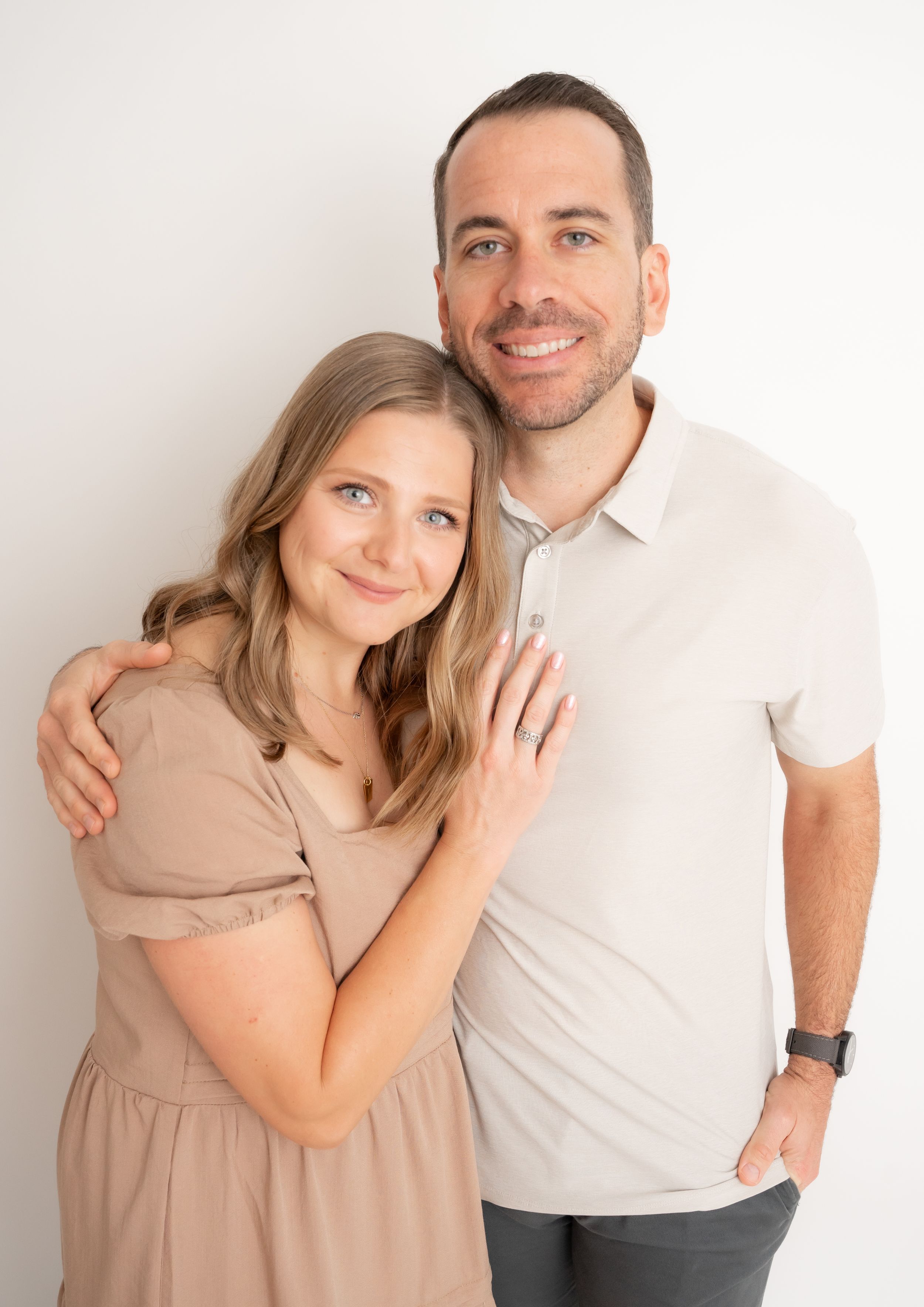 Affectionate couple in beige and white embrace during minimalist studio photoshoot.