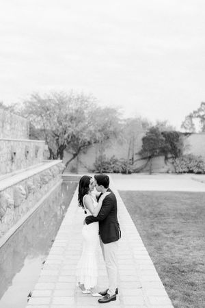 A romantic black and white photo of a couple sharing a tender moment on a stone pathway beside a garden wall.