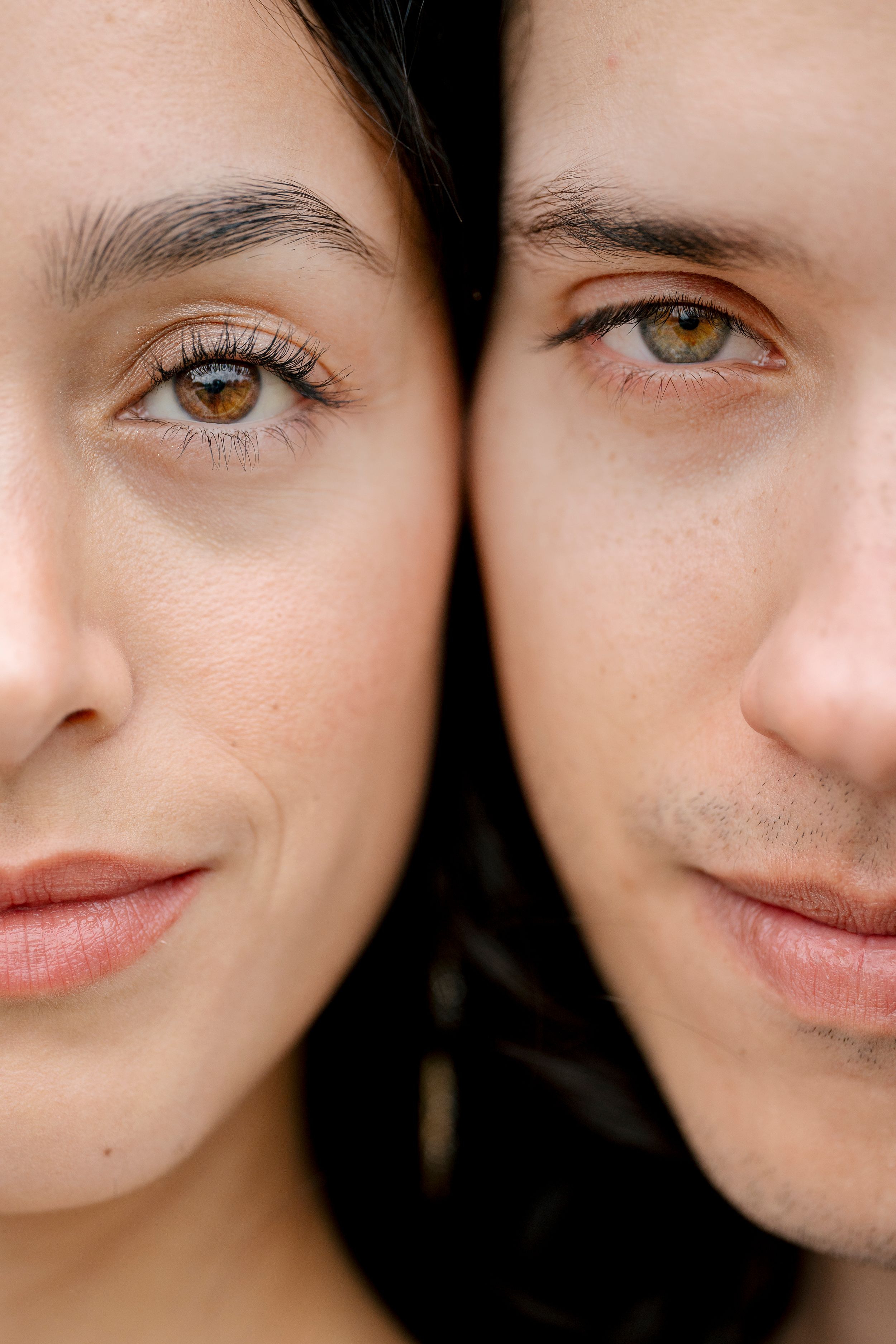 Close up portrait of two faces side by side showing contrasting eye colors and facial features in soft lighting.