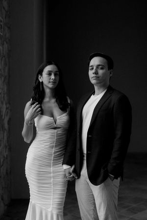 A romantic black and white portrait of a couple in formal attire against a dark background.